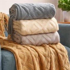 Luxurious folded knitted blankets in grey, cream, and beige on a cozy blue sofa, perfect for home decor and comfort.