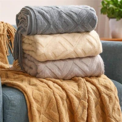Luxurious folded knitted blankets in grey, cream, and beige on a cozy blue sofa, perfect for home decor and comfort.