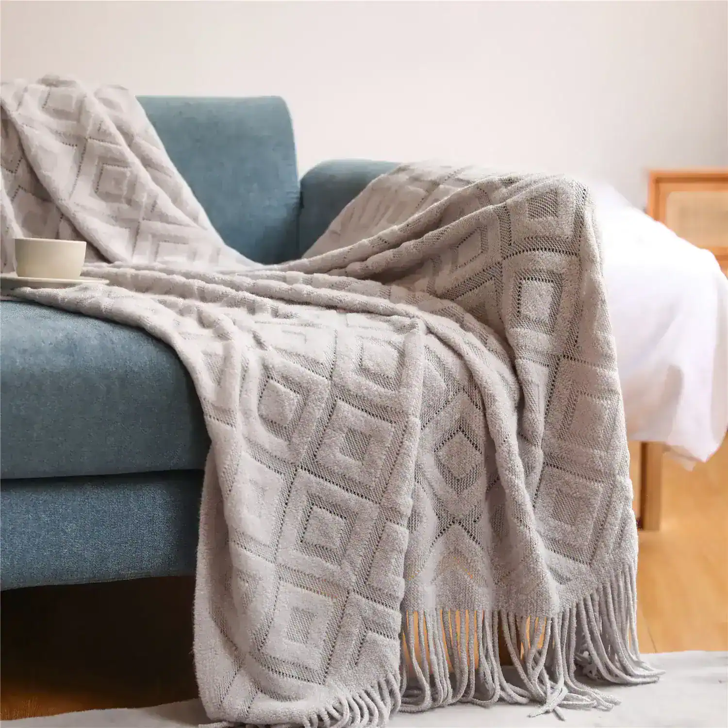 Soft textured beige throw blanket with geometric diamond pattern draped over a modern blue sofa. Perfect for cozy living room decor.