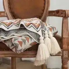 Knitted woven blanket with tassels on vintage wooden armchair for cozy home decor and comfort.