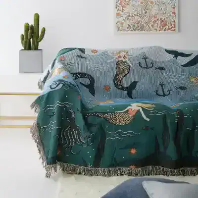 Vibrant ocean-themed tapestry with mermaids, fish, anchors, and sea creatures draped over a sofa in a modern, minimalist living space at Monalisa Store.