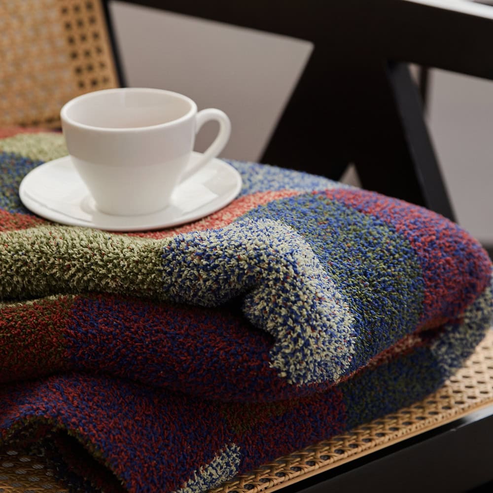 Colorful textured blanket neatly folded on a wooden chair with a white coffee cup and saucer on top for cozy, stylish home decor.