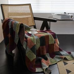 Soft colorful throw blanket draped over modern black wooden chair with rattan backrest in cozy indoor setting, with coffee cup and saucer, sunlit room, perfect for relaxing or reading.