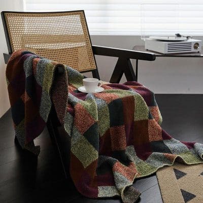 Soft colorful throw blanket draped over modern black wooden chair with rattan backrest in cozy indoor setting, with coffee cup and saucer, sunlit room, perfect for relaxing or reading.