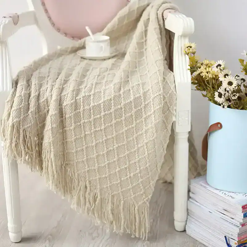 Luxury beige textured throw blanket over white wooden bed frame for cozy bedroom decor, perfect for adding warmth and style, featuring soft tassels and intricate pattern.