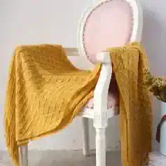 Luxurious mustard yellow textured throw blanket draped over an elegant pink and white antique-style chair, perfect for cozy home decor.