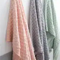 Luxurious chunky knit blankets in pastel pink, grey, and mint green on display at Monalisa Store, perfect for cozying up and adding a touch of elegance to any room.