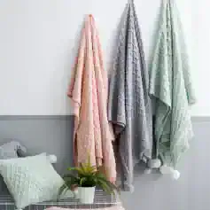 Luxurious cable-knit blankets hanging on wall in pastel pink, grey, and mint green for cozy home decor at Monalisa Store, perfect for adding warmth and style to your living space.