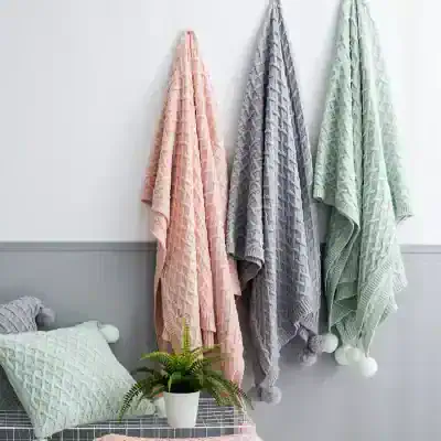 Luxurious cable-knit blankets hanging on wall in pastel pink, grey, and mint green for cozy home decor at Monalisa Store, perfect for adding warmth and style to your living space.