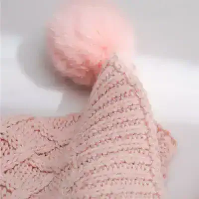 Soft pink knitted hat with a fluffy pom-pom, perfect for cold weather and winter fashion accessories. Elegant and cozy for children and adults.