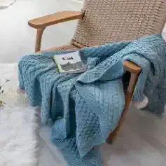 Soft blue knitted throw blanket draped over a wooden chair with a cat-themed book on top, creating a cozy and inviting reading corner at Monalisa Medical Store.