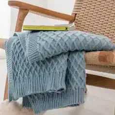 Luxury blue cable knit sweater draped over rattan armchair with books on top, cozy home decor, stylish casual fashion, perfect for cold weather, Monalisa Store opt.