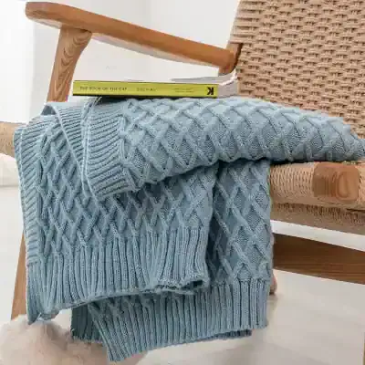 Luxury blue cable knit sweater draped over rattan armchair with books on top, cozy home decor, stylish casual fashion, perfect for cold weather, Monalisa Store opt.