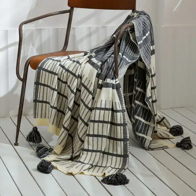 Modern geometric patterned throw blanket draped over vintage wooden and metal chair, stylish home decor accent, monochrome design, perfect for contemporary interior styling.