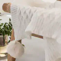 Soft white knitted socks with ribbed texture and fluffy pom-pom detail, perfect for cozy comfort and stylish loungewear. Ideal for winter warmth or as a fashionable accessory.