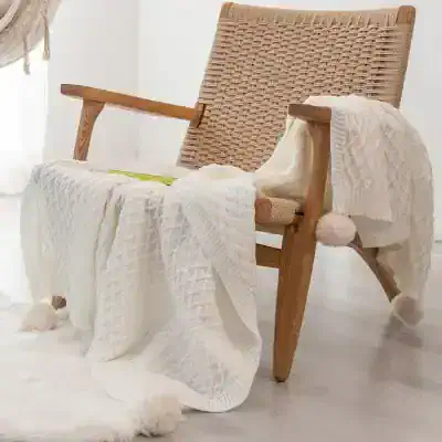 Luxurious cozy knit blanket with pom-pom accents draped over modern wooden armchair, perfect for NAPA special gifts at Monalisa Medical Store.