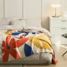 Colorful floral blanket on a cozy white bed in a modern bedroom with white furniture and soft lighting, perfect for a relaxing sleep environment.