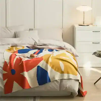 Colorful floral blanket on a cozy white bed in a modern bedroom with white furniture and soft lighting, perfect for a relaxing sleep environment.