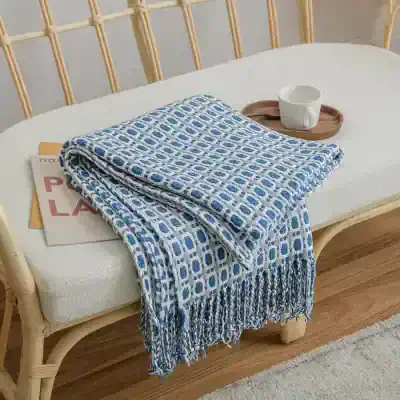 Soft blue and white patterned throw blanket with fringe, perfect for cozy home decor and gifting, on a rattan bench in a modern living space.