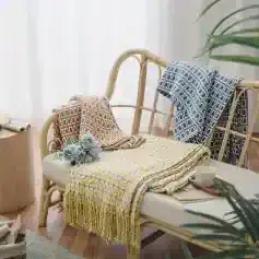 Soft pastel-colored woven throw blankets and matching scarves displayed on a rattan bench with a cozy, inviting atmosphere perfect for home decor and comfort.