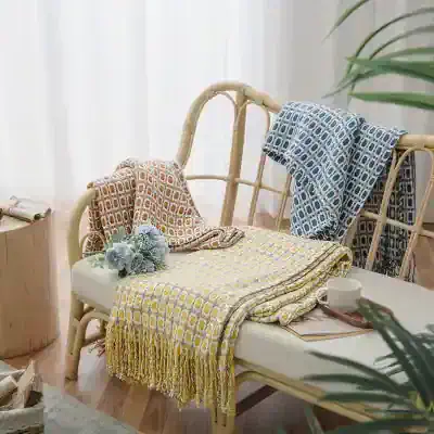 Soft pastel-colored woven throw blankets and matching scarves displayed on a rattan bench with a cozy, inviting atmosphere perfect for home decor and comfort.