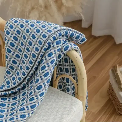 Luxurious blue and white patterned textile draped over rattan chair in a cozy, modern interior setting. Perfect for home decor or comfort.