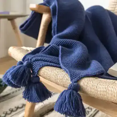 Blue tasseled throw blanket on woven bench, cozy home decor, luxury textile, stylish comfort, Monalisa Store, premium quality, elegant living, modern interior design, soft and warm fabric, decorative blanket, fashionable home accessories, premium home textiles, Monalisa Medical Store, home fashion, interior accessories.