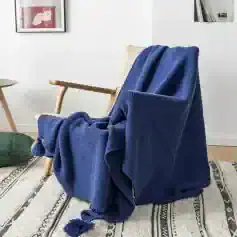 Luxurious blue throw blanket draped over a modern wooden armchair in a cozy living room, perfect for enhancing comfort and style.