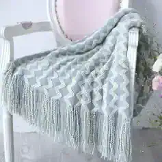 Soft gray and cream woven throw blanket with tassel fringe on a vintage-style white vanity table, ideal for cozy home decor and naps.