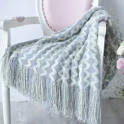 Soft gray and cream woven throw blanket with tassel fringe on a vintage-style white vanity table, ideal for cozy home decor and naps.