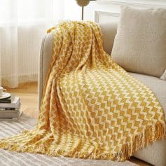 Vibrant yellow and white geometric patterned blanket draped over a beige sofa in a cozy living room setting. Perfect for adding color and style to your home decor.