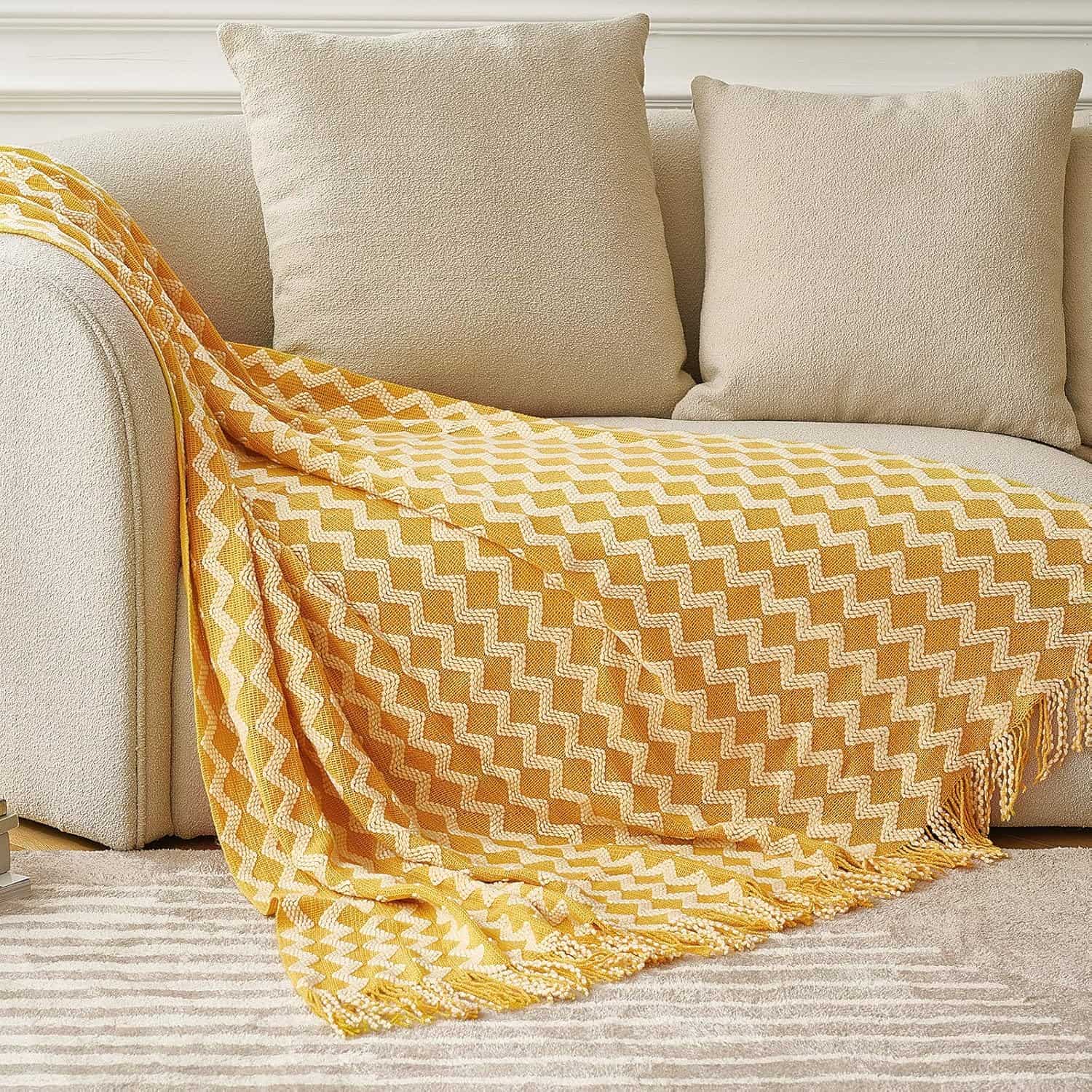 Soft beige sofa with a yellow and white zigzag patterned throw blanket and matching cushions, creating a cozy and stylish living space.