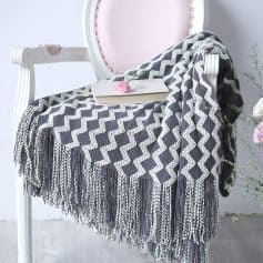 Soft gray and white geometric patterned throw blanket on elegant white chair with pink cushioned back, book and flower, cozy home decor, Monalisa Store.