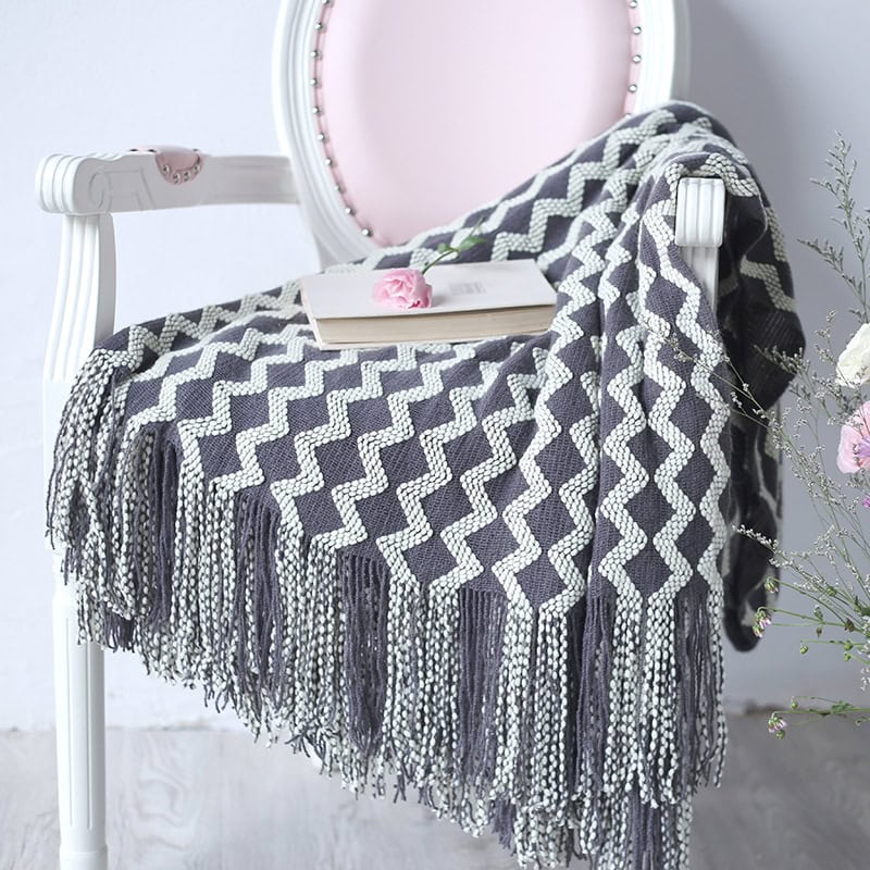 Soft gray and white geometric patterned throw blanket on elegant white chair with pink cushioned back, book and flower, cozy home decor, Monalisa Store.