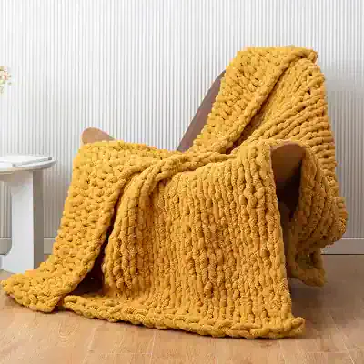 Chunky yellow knitted blanket draped over a modern armchair in a cozy living space, perfect for home decor and relaxation, featured on Monalisa Medical store.