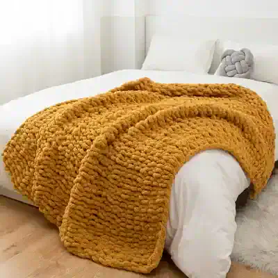 Plush mustard yellow chunky knit blanket on a modern white bed, cozy and stylish bedroom decor for comfort and warmth.