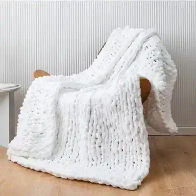 Luxurious white faux fur blanket draped over a wooden chair, perfect for cozy home decor and comfort.
