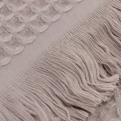 Soft beige woven textile with intricate cable knit patterns and fringed edges, perfect for cozy scarves, throws, or home decor. High-quality fabric designed for comfort and style.