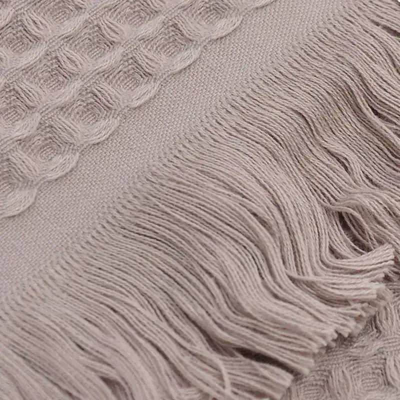 Soft beige woven textile with intricate cable knit patterns and fringed edges, perfect for cozy scarves, throws, or home decor. High-quality fabric designed for comfort and style.