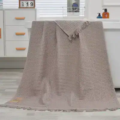 Luxurious beige waffle knit throw blanket draped over a countertop with modern kitchen background. Perfect for cozy home decor or as a stylish gift. Soft, textured, and high-quality fabric.