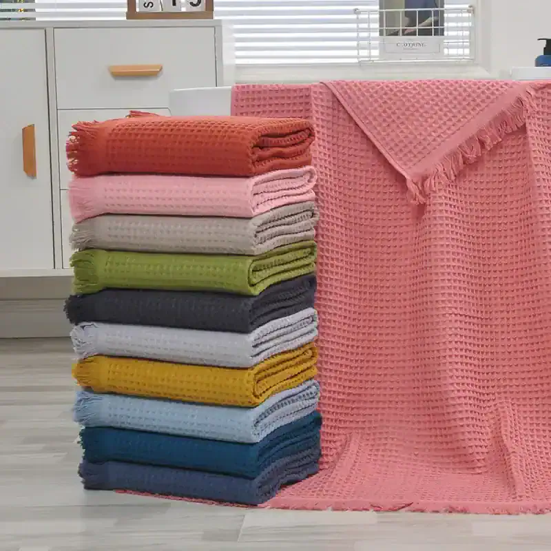 Soft pastel and vibrant colored towels stacked neatly on a wooden floor in a cozy, modern home setting, with an additional towel draped over a table, showcasing high-quality textiles for home and bath decor.