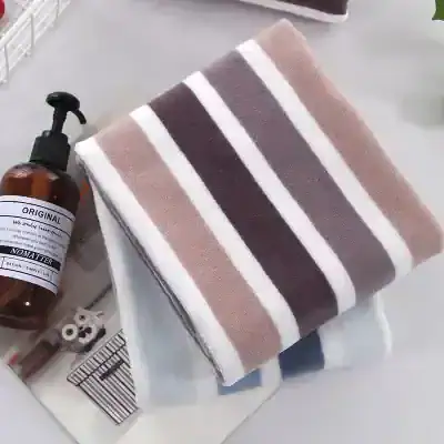 Soft striped towel in neutral tones laid on a white surface with a brown pump bottle nearby.