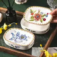 Colorful floral patterned ceramic storage boxes with lids, ideal for home decor and organization, displayed on a wooden tray with yellow flowers and a diffuser.