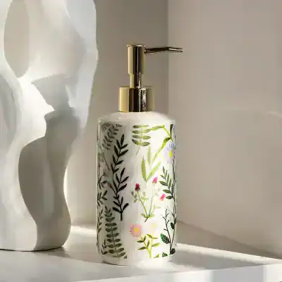 White floral patterned liquid soap dispenser with gold pump on a light-colored surface. Perfect for bathroom or kitchen decor, combining elegance and nature-inspired design.