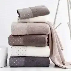 Soft plush towels in neutral colors stacked on a white surface with a minimalist background.