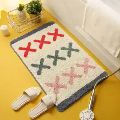 Shower room rug with colorful X patterns, positioned on a bright yellow floor next to slippers and bathroom essentials, highlighting cozy and stylish home decor.