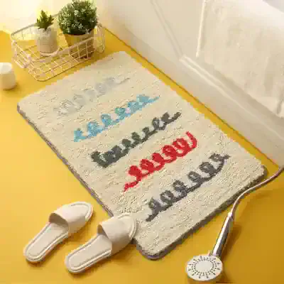 Colorful bathroom rug with playful word patterns in blue, black, red, and gray decorates a yellow bathroom floor, featuring a white slippers, a shower head, and small potted plants, creating a cozy and inviting space for relaxation and self-care.
