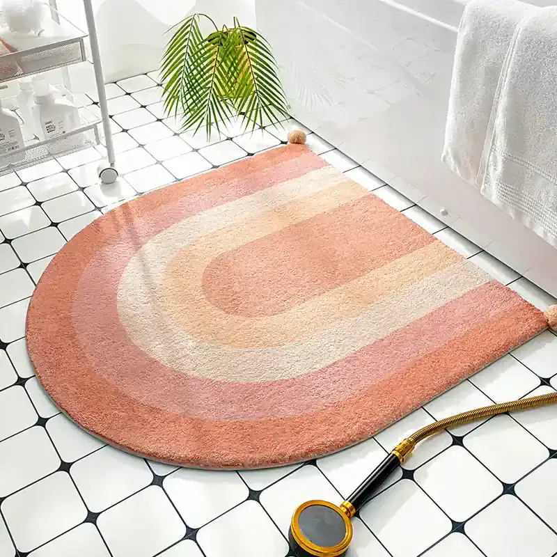 Pink and beige oval area rug on white tiled bathroom floor, with a shower hose, towel, and plants, adding a stylish, cozy touch to modern bath decor.