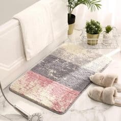 Plush bathroom rug with pink, gray, and white color blocks, placed on a marble floor in a modern, minimalist bathroom setting.