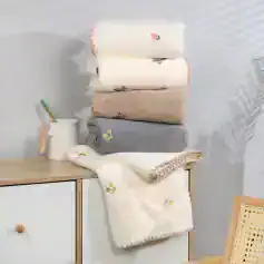 Soft pastel towels with floral embroidery and textured accents at Monalisa Store, perfect for optometry and eyewear styling, displayed on a minimalist wooden surface.